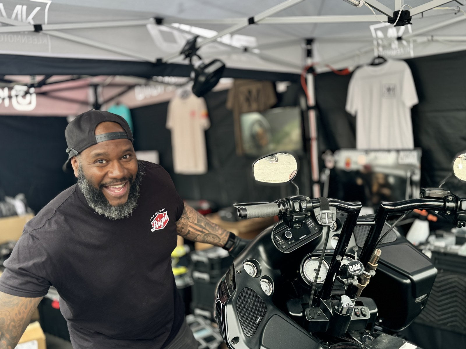 KLEENMOTO rider smiling beside a black Harley at an event booth